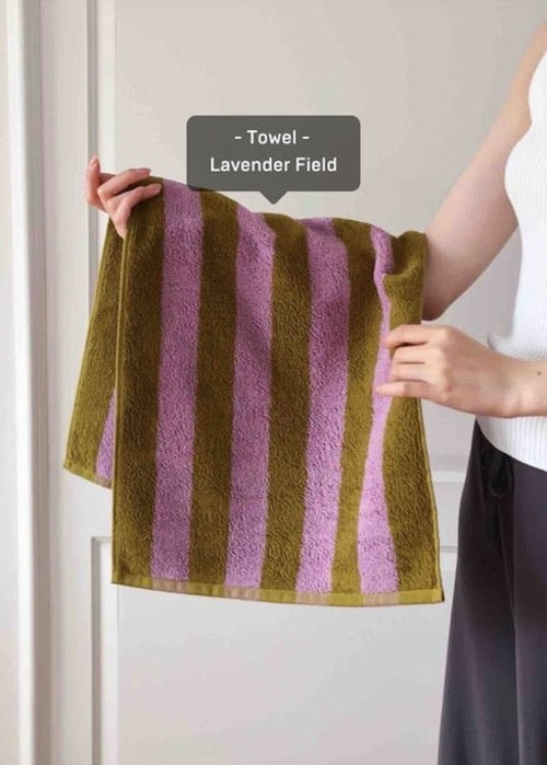 Person holding a striped towel labeled 'Lavender Field' against a neutral background